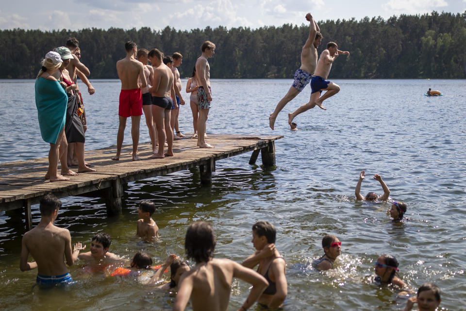 People enjoy the warm weather near a lake near Vilnius, Lithuania, Sunday, June 20, 2021. The hot weather continues in Lithuania as temperatures reached 33 degrees Celsius (91,40 degrees Fahrenheit). (AP Photo/Mindaugas Kulbis)