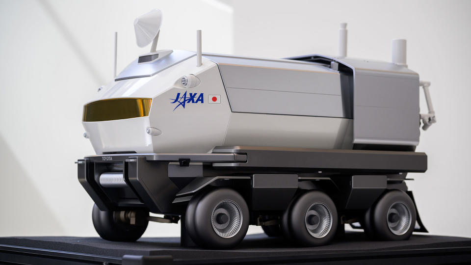 A model of a large six-wheeled white lunar rover rests on a table