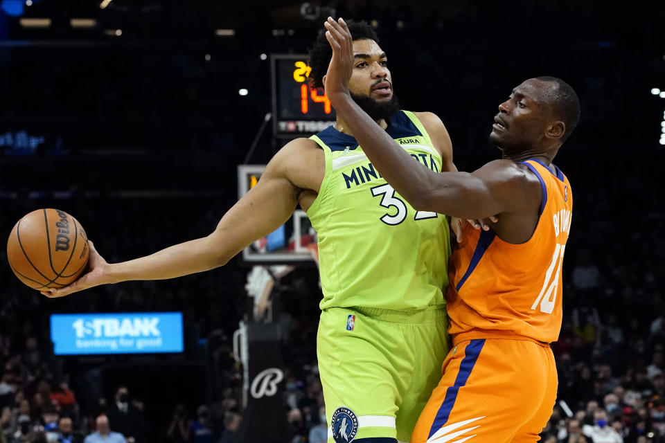 Minnesota Timberwolves center Karl-Anthony Towns (32) looks to pass as Phoenix Suns center Bismack Biyombo (18) defends during the first half of an NBA basketball game, Friday, Jan. 28, 2022, in Phoenix. (AP Photo/Matt York)