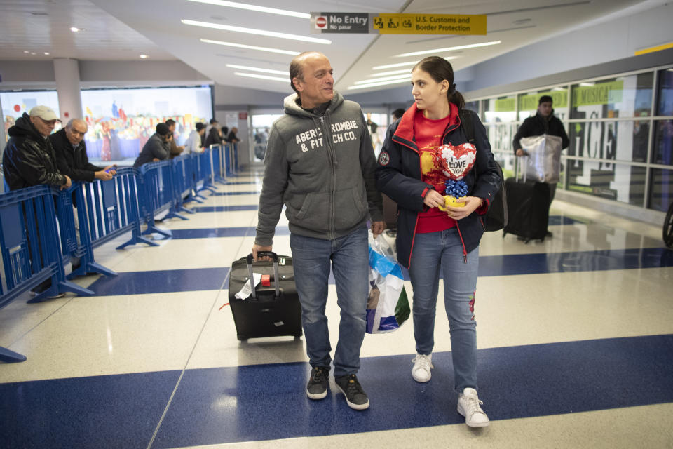 In this Tuesday, Dec. 3, 2019, photo Mohammed Hafar, left, helps his daughter Jana with her luggage as they leave JFK Airport in New York. Jana had been forced by President Donald Trump's travel ban to stay behind in Syria for months while her father, his wife and son Karim started rebuilding their lives in Bloomfield, N.J., with no clear idea of when the family would be together again. Mohammed was part of a federal lawsuit filed in August of this year over the travel ban waiver process. (AP Photo/Mary Altaffer)