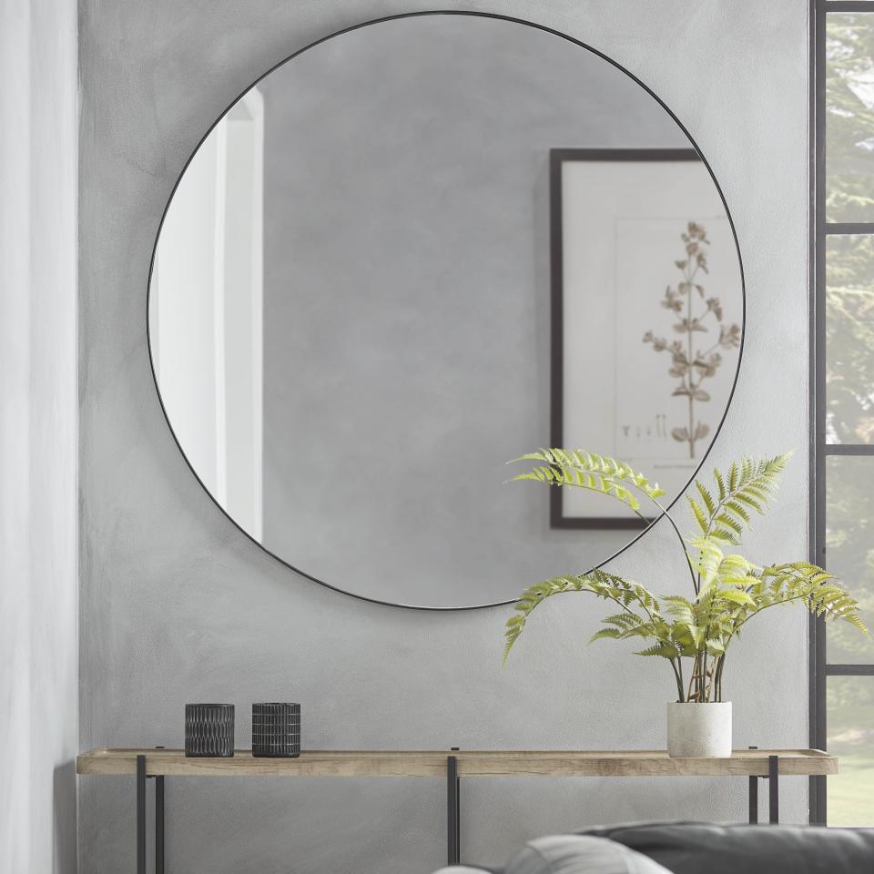 round mirror with black frame on wall above console table