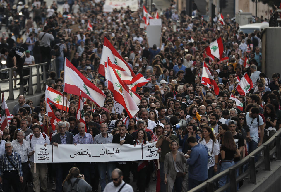 Anti-government protesters march during a protest against the central bank and the Lebanese government, in Beirut, Lebanon, Thursday, Oct. 31, 2019. Lebanese security forces were still struggling to open some roads Thursday as protesters continued their civil disobedience campaign in support of nationwide anti-government demonstrations. The Arabic banner, front, reads:"Lebanon rises up." (AP Photo/Hussein Malla)