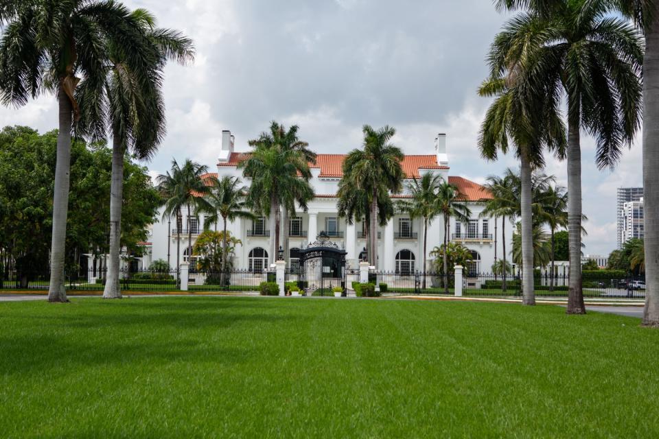 A white mansion known with a large green lawn and palm trees