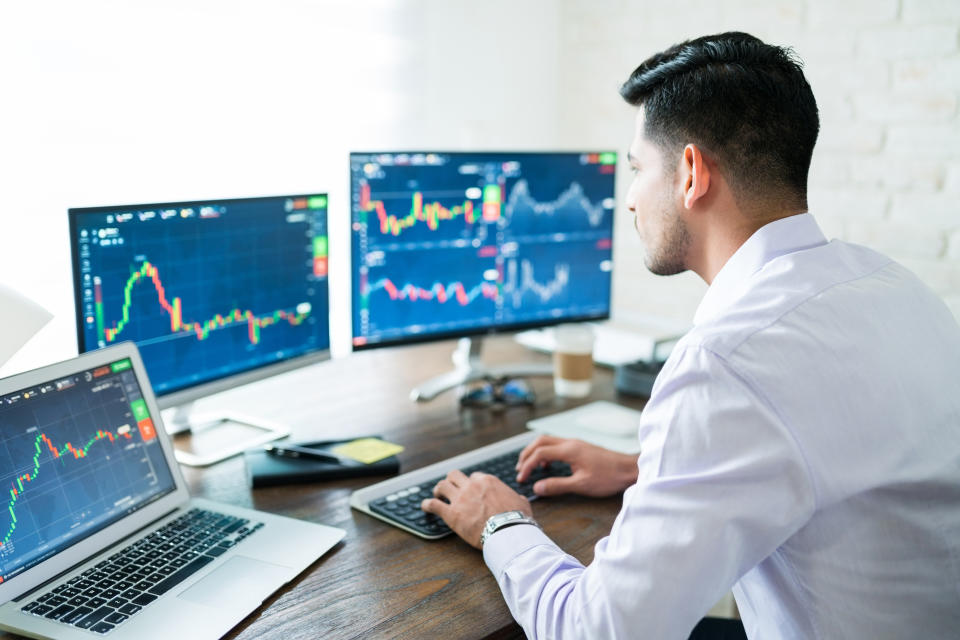 Hispanic young male stock trader typing on keyboard while using computer at home