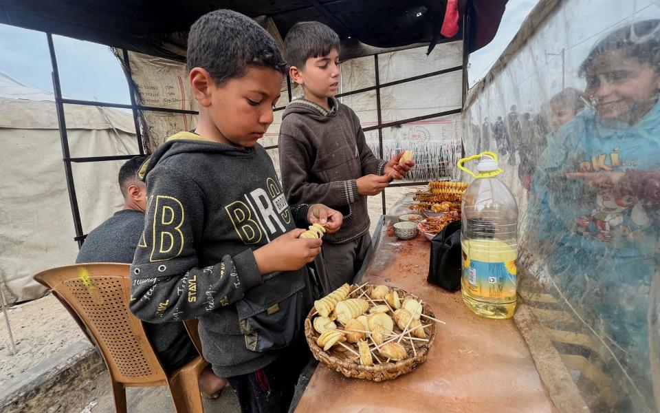 Displaced Palestinian boys sell homemade potato chips outside a tent camp