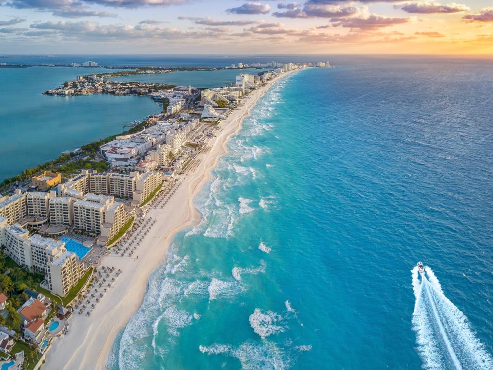 an aerial shot of Cancun, Mexico with a boat in the water next to the sunset.