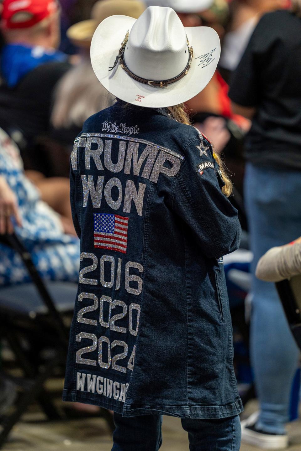 An attendee stands up wearing a bedazzled jean jacket stating Trump won 2016, 2020, and 2024 on the back, during a Trump rally at the Van Andel Arena in Grand Rapids on Saturday, July 20, 2024.
