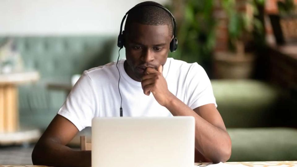 Young black man sitting in front of laptop while wearing headphones