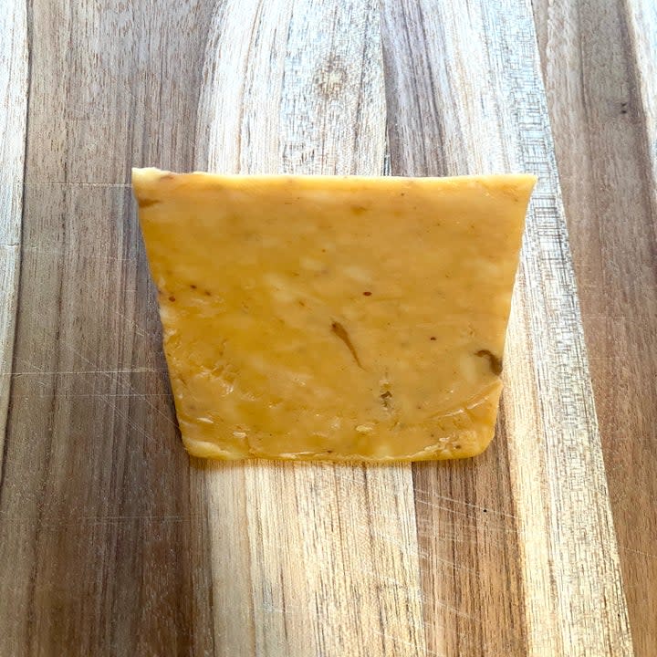 A wedge of Figgy Cheddar on a wooden cutting board