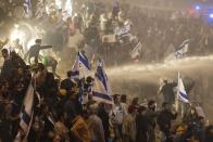 Israeli police use a water cannon to disperse demonstrators blocking a highway during a protest against plans by Prime Minister Benjamin Netanyahu's government to overhaul the judicial system in Tel Aviv, Israel, Monday, March 27, 2023. Tens of thousands of Israelis have poured into the streets across the country in a spontaneous outburst of anger after Prime Minister Benjamin Netanyahu abruptly fired his defense minister for challenging the Israeli leader's judicial overhaul plan. (AP Photo/Oren Ziv)