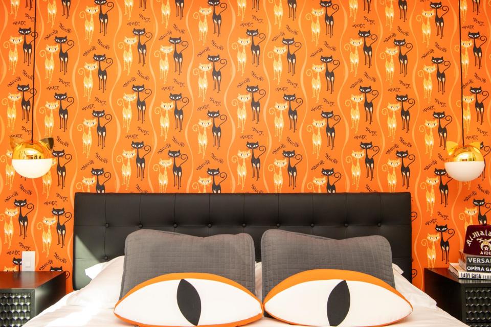 A cat-themed bedroom in the Shag House has cats on the wallpaper and cat's-eye-shaped pillows on the bed.