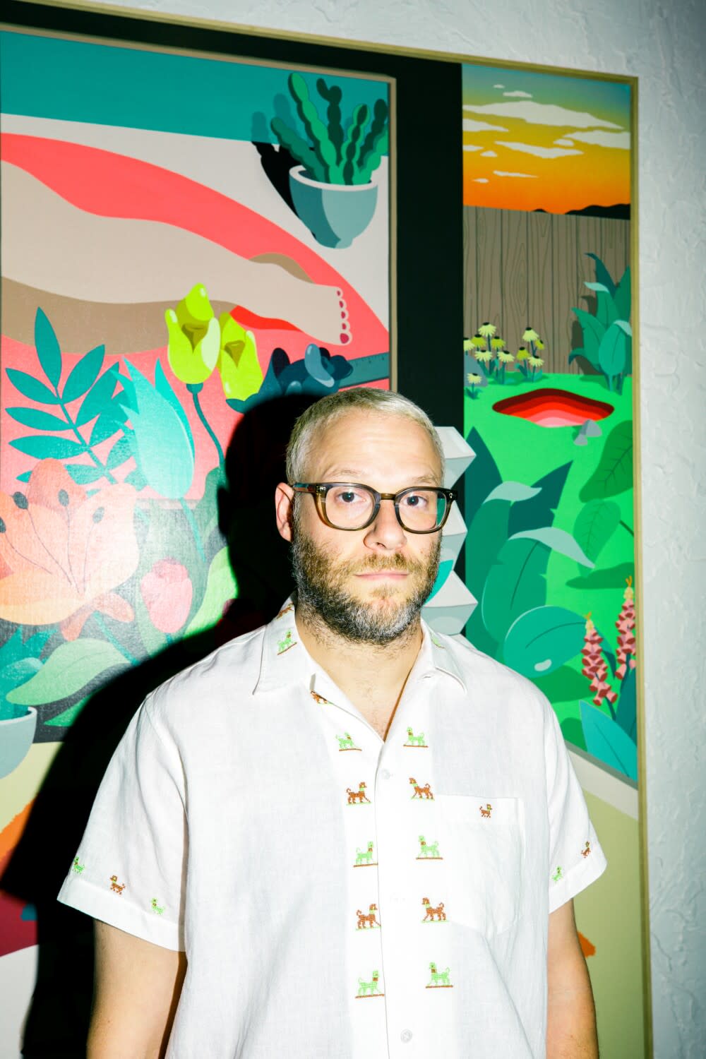 A man with close-shaved hair stands in front of a painting for his portrait.