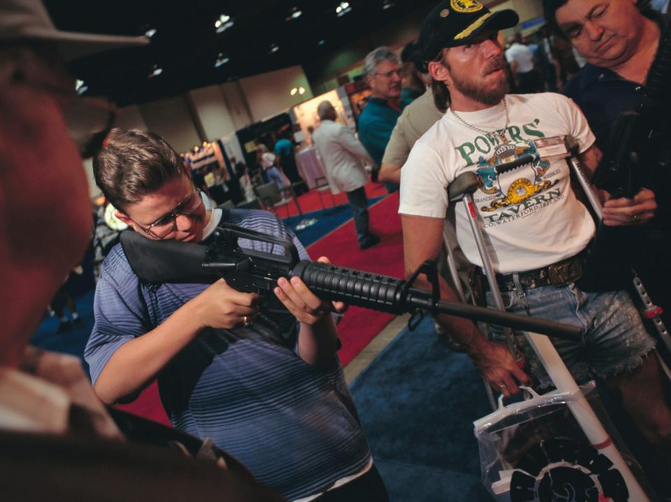 A person holds gun while others look at guns at an NRA convention in 1995.