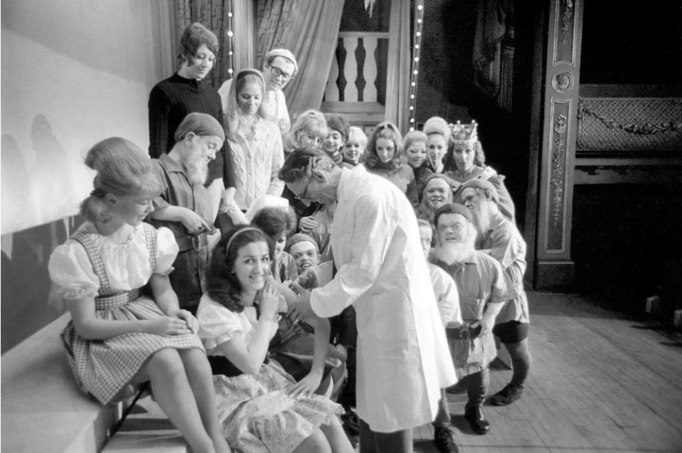 A doctor with his syringe makes ready to give anti-flu vaccine to Margaret Ayre, who plays Snow White and the rest of the cast at the City Varieties, Leeds in December 1969.