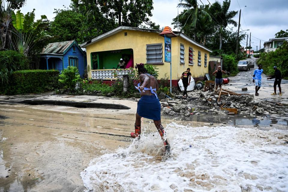 <p>A woman runs as water from the sea floods a street after the passage of Hurricane Beryl in the parish of Saint James, Barbados</p> (AFP via Getty Images)