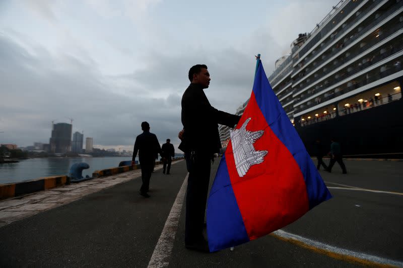 A man holds a Camboadian flag as MS Westerdam, a cruise ship that spent two weeks at sea after being turned away by five countries over fears that someone aboard might have the coronavirus, docks in Sihanoukville