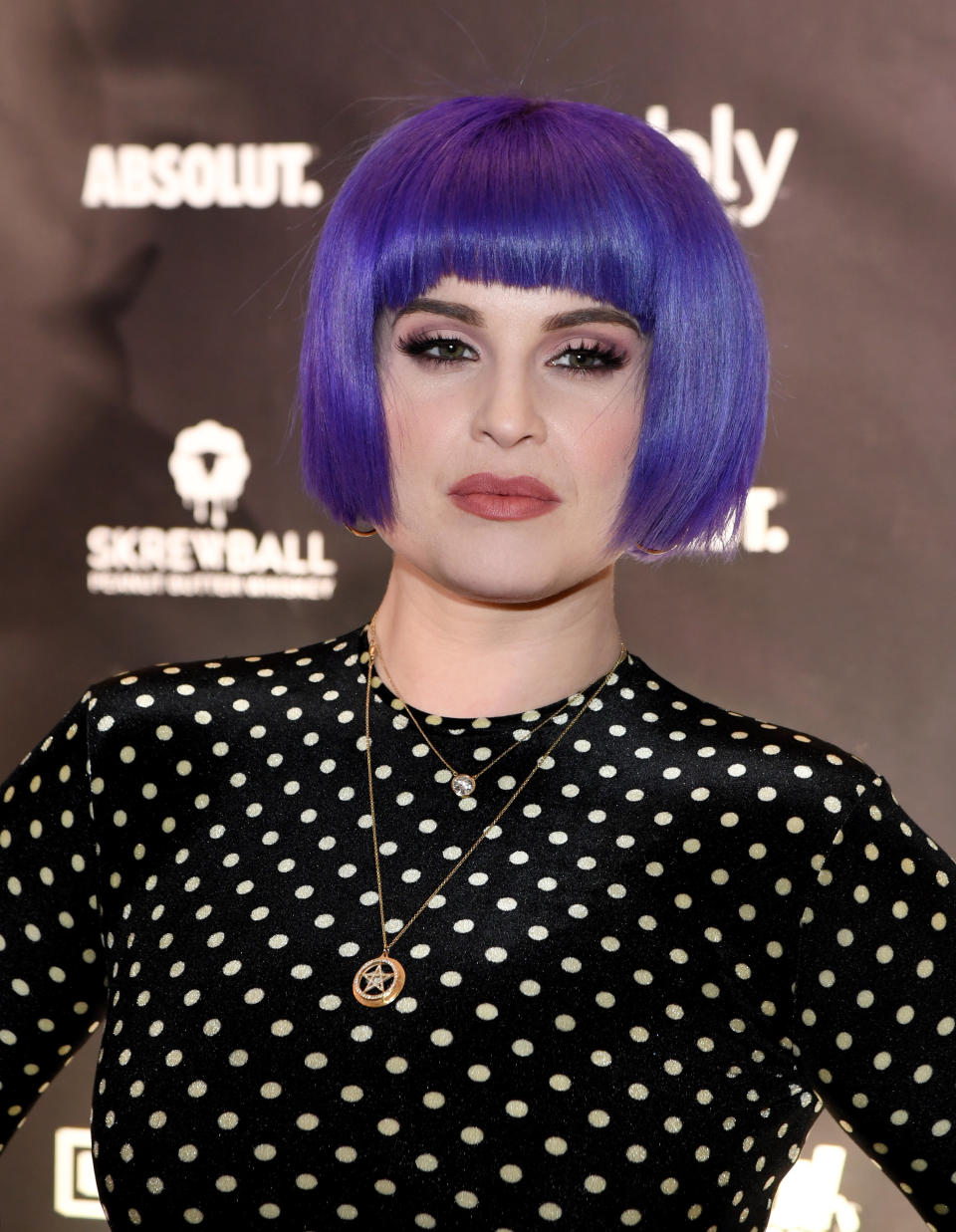 Kelly wearing a polka dot top and two necklaces as she poses for photographers at a red carpet event