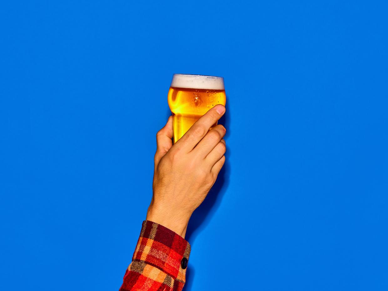 A man raises a pint of beer into the air, against a blue background.