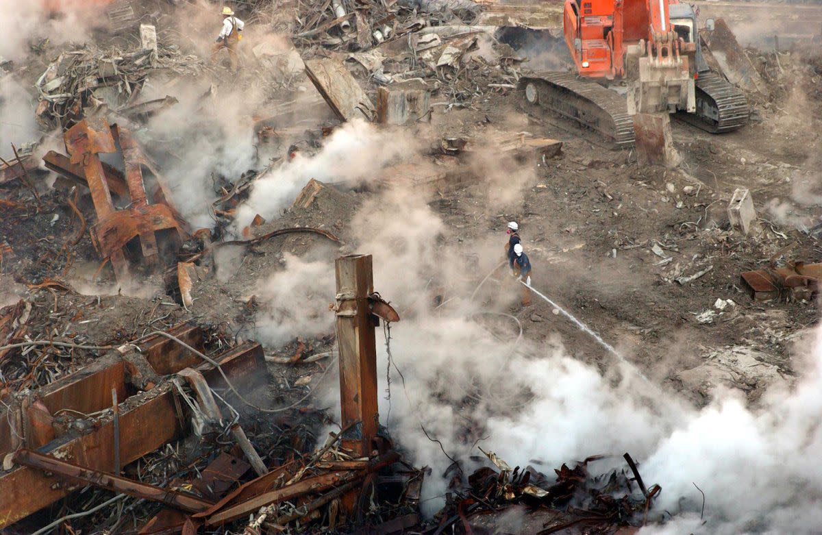 In this file photo of Oct. 11, 2001, twisted steel juts out from the rubble of the north World Trade Center tower in New York as a firefighter tries to cool down the still smoldering debris one month to the day after the disaster. 