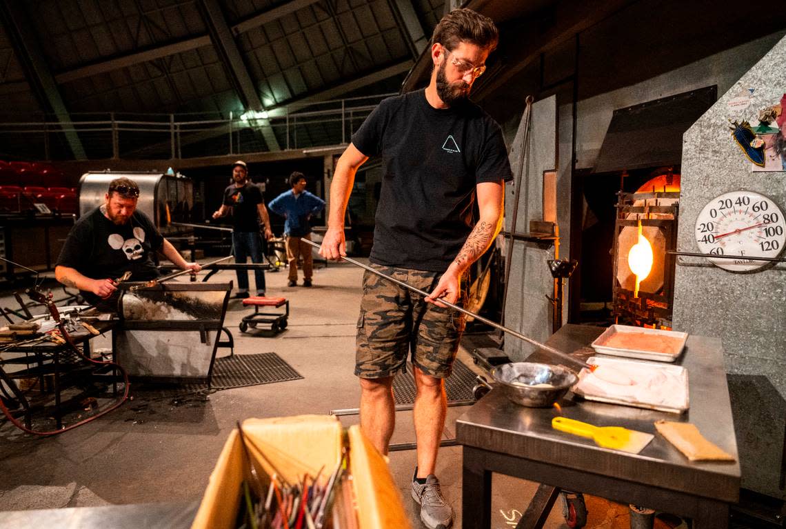 Museum of Glass hot shop director and lead gaffer Benjamin Cobb places a hot piece of glass in colored sand to make it pink while working in the hot shop at the museum in Tacoma, Wash. on Nov. 10, 2022.