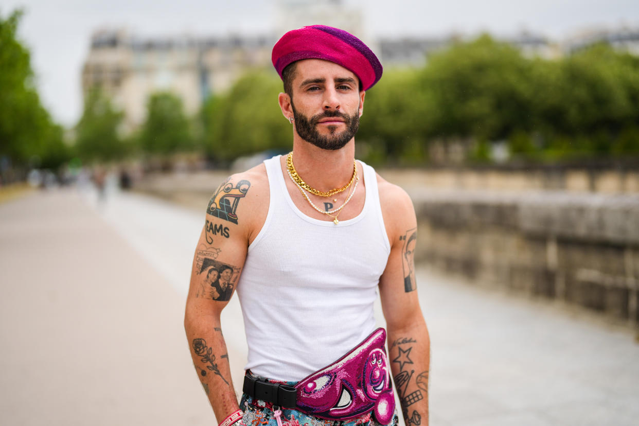 PARIS, FRANCE - JUNE 25: Pelayo Diaz wears gold earrings, a fuchsia / purple /and white print patter wool felt beret / hat, a gold chain necklace, a white pearls necklace, gold chain necklaces, a white ribbed tank-top, a navy blue Christian Dior bracelet from Dior, a gold Juste Un Clou bracelet from Cartier, silver and gold bracelets, a gold ring, a pale blue / red and fuchsia multicolored print pattern flowing large pants, a large white and pink pearl belt with patterns and a pompom, a silver watch, a red Christian Dior bracelet from Dior, outside Dior, during Paris Fashion Week - Menswear Spring/Summer 2022, on June 25, 2021 in Paris, France. (Photo by Edward Berthelot/Getty Images)