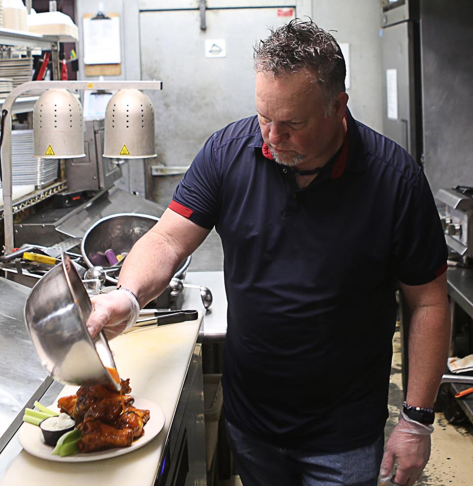 Tom Craft pours sauce over a plate of chicken wings at 2 Fat Guys American Grill in Hockessin on Friday, April 12, 2024.