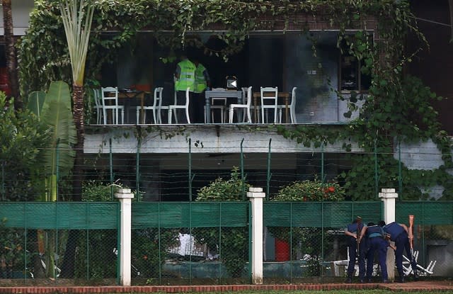 Policemen sneak a look inside the Holey Artisan Bakery and the O'Kitchen Restaurant as others inspect the site after gunmen attacked in Dhaka