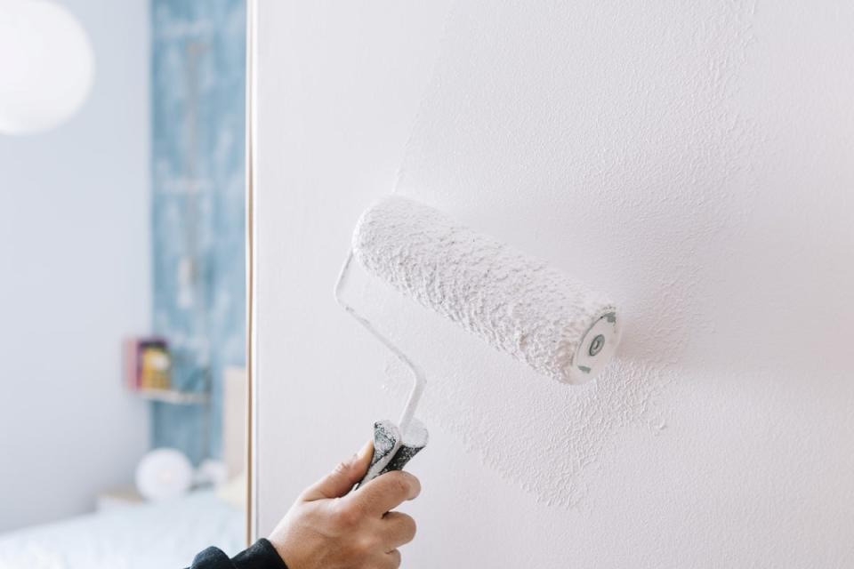 Person rolling white paint or primer on a white wall
