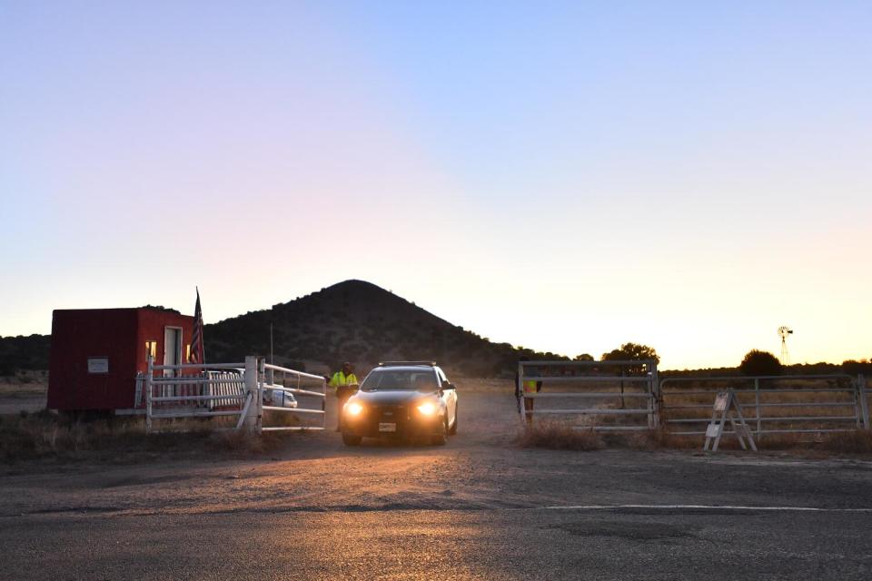 A police car exits a gated ranch as the sun sets.