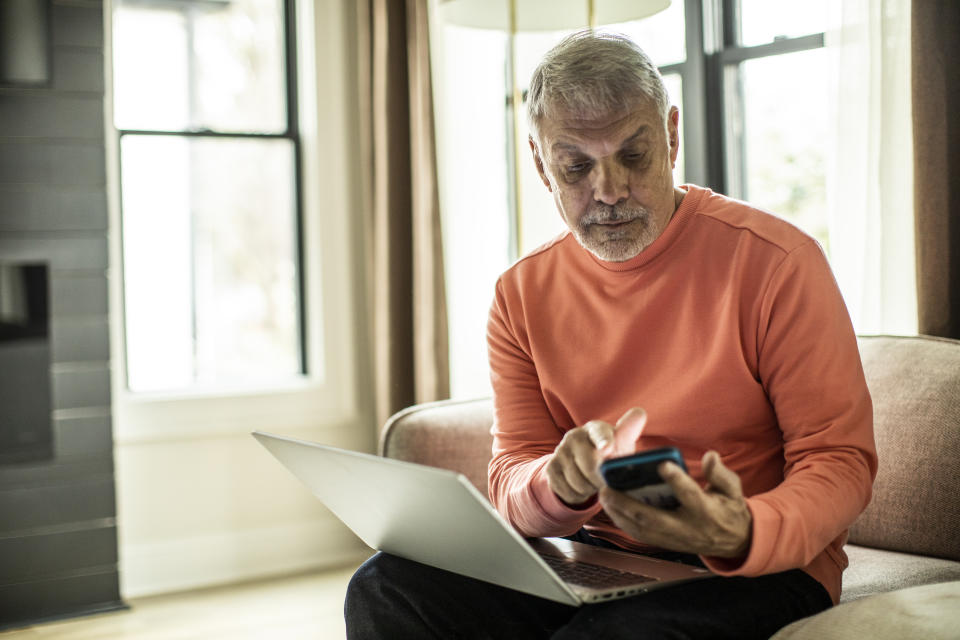 Senior man using laptop computer and smartphone at home