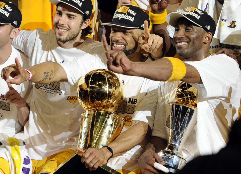 Los Angeles Lakers guard Derek Fisher, center, holds the Larry O'Brien Trophy as Kobe Bryant, right, holds the MVP trophy as they celebrate after beating the Boston Celtics, 83-79, in Game 7 of the NBA basketball finals in Los Angeles, June 17, 2010. At second left is Lakers' Sasha Vujacic. Bryant, the 18-time NBA All-Star who won five championships and became one of the greatest basketball players of his generation during a 20-year career with the Los Angeles Lakers, died in a helicopter crash Sunday, Jan. 26, 2020. (AP Photo/Mark J. Terrill)