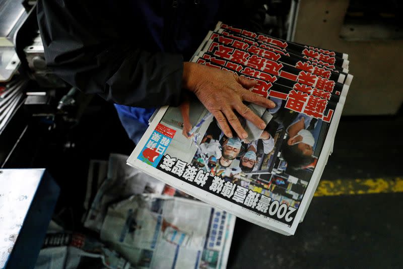 An employee takes copies of the Apple Daily newspaper, published by Next Media Ltd, with a headline "Apple Daily will fight on", in Hong Kong