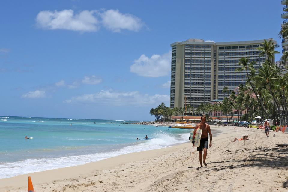 In this June 5, 2020, file photo, a surfer walks on a sparsely populated Waikiki Beach in Honolulu. Hawaii's governor says that starting Oct. 15, travelers arriving from out of state may bypass a 14-day quarantine requirement if they test negative for COVID-19.