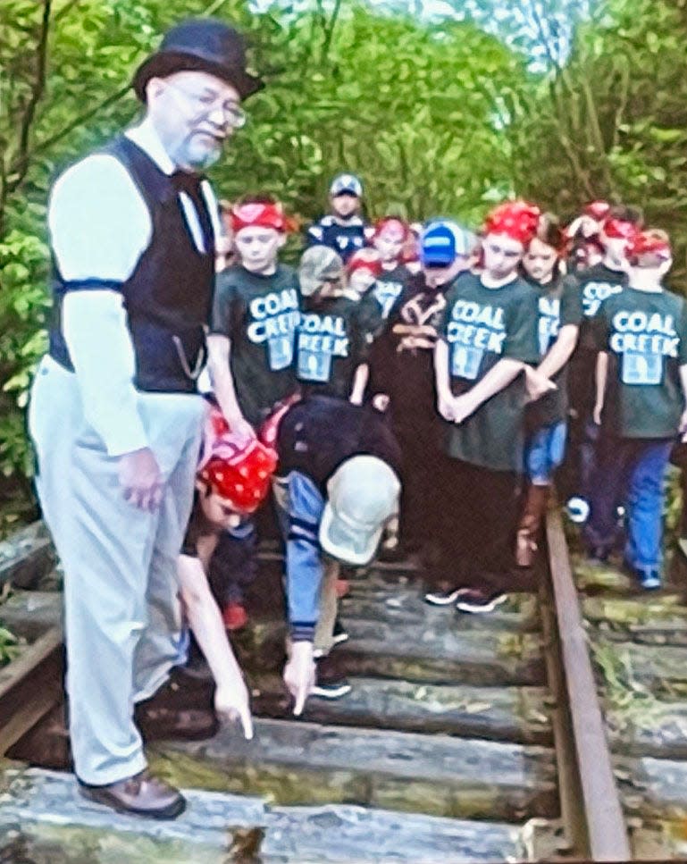 Barry Thacker, dressed as Welsh coal miner David Thomas, speaks to a group of Coal Creek Scholars. Two students are pointing to the notches in the crosstie where the rope was placed for the hanging of David Drummond.