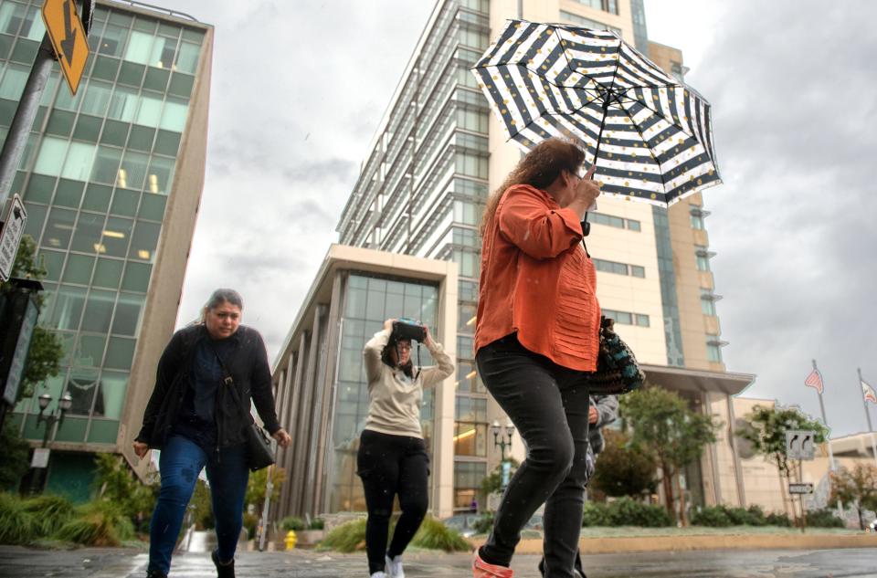 Pedstirans use any means they can to stay dry  from the first rain of the season as they cross Weber Avenue at Hunter Street in downtown Stockton on Tuesday, Nov. 1, 2022.
