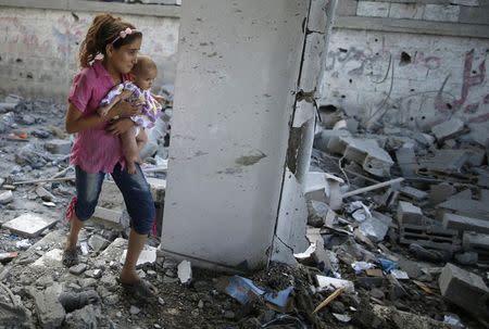 A Palestinian girl holding her sister walks through debris near remains of a mosque, which witnesses said was hit by an Israeli air strike, in Beit Hanoun in the northern Gaza Strip August 25, 2014. REUTERS/Mohammed Salem