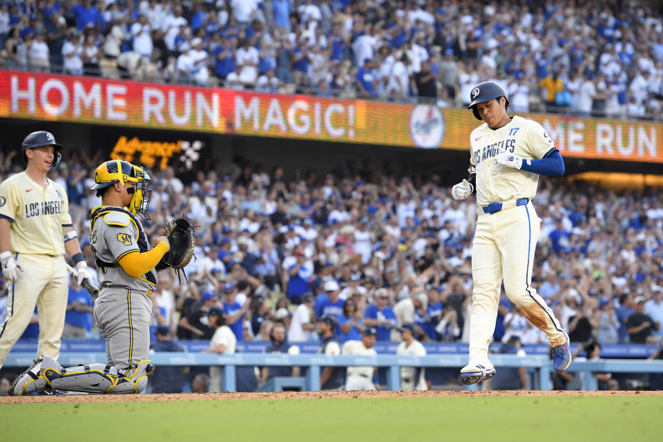 Los Angeles Dodgers' Shohei Ohtani, right, scores after hitting a solo home run as Will Smith, left, and Milwaukee Brewers catcher William Contreras stand by during the eighth inning of a baseball game Saturday, July 6, 2024, in Los Angeles. (AP Photo/Mark J. Terrill)