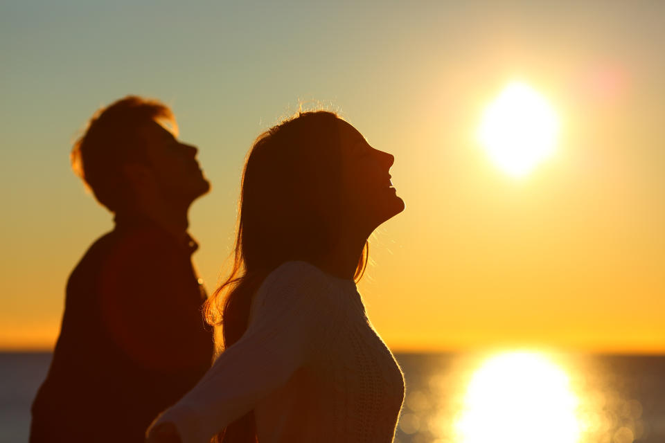 Silhouette of a couple of friends breathing deep fresh air at sunset on the beach