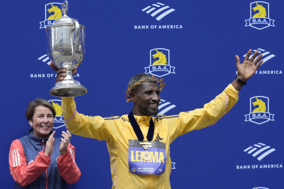 Sisay Lemma, of Ethiopia, right, winner of the men's division of the Boston Marathon displays the trophy as Mass. Gov. Maura Healey, left, applauds during ceremonies, Monday, April 15, 2024, in Boston. (AP Photo/Steven Senne)