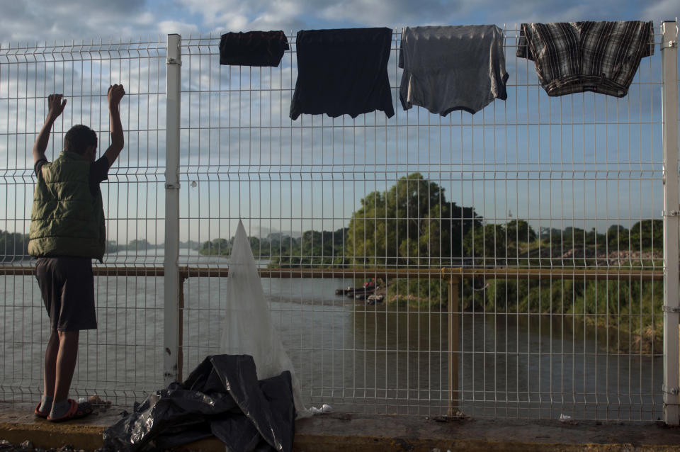 A Honduras migrant looks over the Suchiate River, which separates Mexico, right, and Guatemala, left, as he stands on a bridge covered by drying clothes in Tecun Uman, Guatemala, at sunrise Sunday, Oct. 21, 2018, near Mexico's Ciudad Hidalgo. Despite Mexican efforts to stop them at the border, about 5,000 Central American migrants resumed their advance toward the U.S. border early Sunday in southern Mexico. (AP Photo/Oliver de Ros)