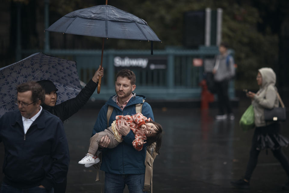 A guardian carries a child as his partner holds the umbrellas following heavy rains on Friday, Sept. 29, 2023, in New York. (AP Photo/Andres Kudacki)