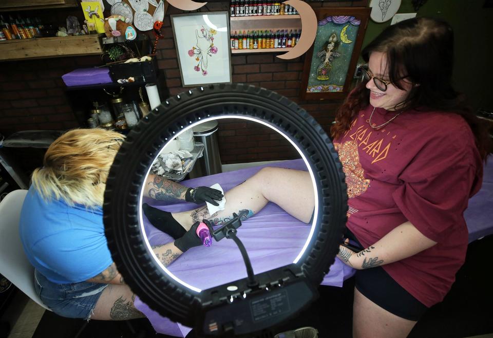 Abby Star of Cleveland, right, is all smiles as she watches Slinkii tattoo her leg during Black Amethyst Tattoo Co.'s during the shop's flash sale to raise money for local abortion funds on Monday.