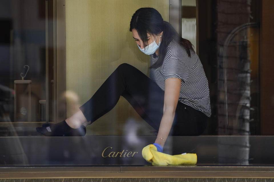 A woman wearing a face mask cleans a display case at Cartier on Rodeo Drive during the coronavirus pandemic Tuesday, May 19, 2020, in Beverly Hills, Calif. (AP Photo/Ashley Landis)