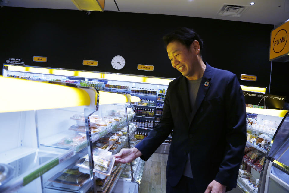 FamilyMart Executive Officer Tomohiro Kano looks at a packed lunch at a FamilyMart convenience store in Tokyo, Friday, Aug. 26, 2022, where the TX SCARA robot is stocking shelves with bottles and cans. The robot can restock shelves with up to 1,000 bottles and cans a day. (AP Photo/Yuri Kageyama)