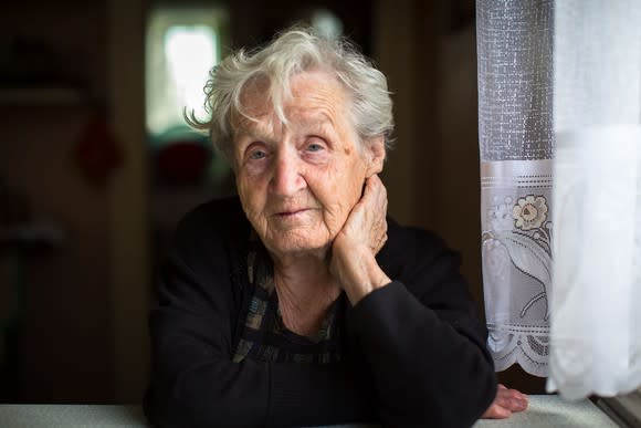 Elderly woman sitting at table holding her face up with her hand