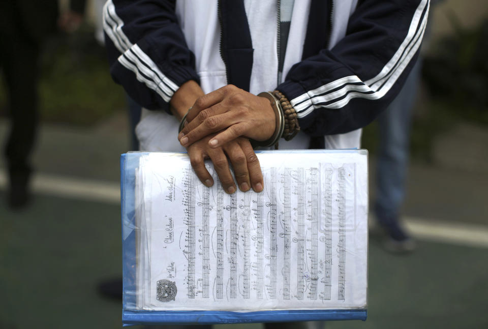 In this July 19, 2019 photo, a handcuffed inmate holds a sheet of music in a prison courtyard in Callao, Peru, as he waits to be transported to a classical music session with a symphony orchestra in the national theater in the Peruvian capital. The excursion is part of a pioneering project to rehabilitate criminals, some convicted of murder, robbery and drug trafficking. (AP Photo/Martin Mejia)