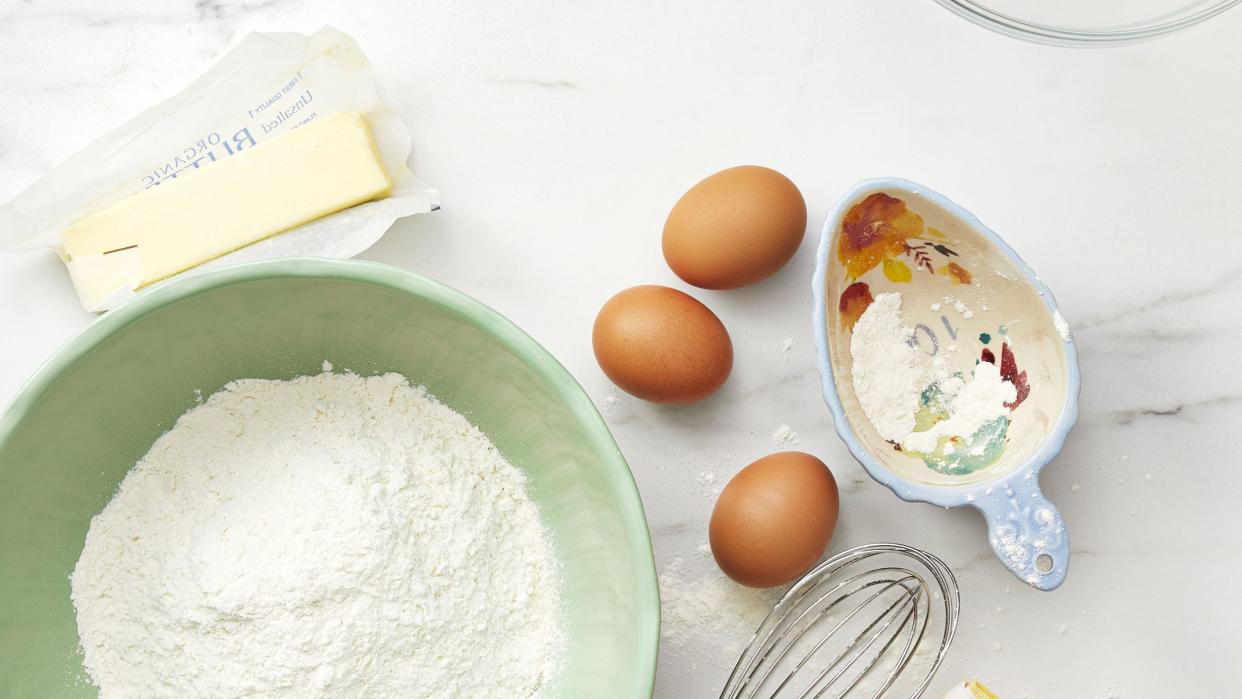 baking ingredients on kitchen counter   flour, butter, eggs, whisk