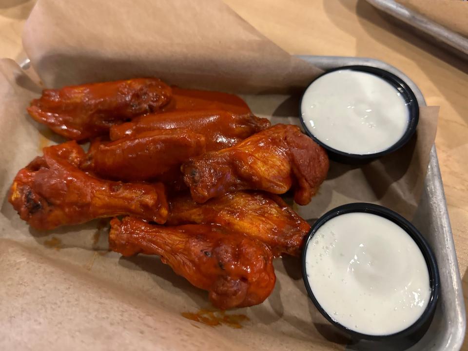 Bone-in chicken wings with sauce on them with two cups of blue cheese sauce