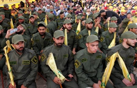 Lebanon's Hezbollah members hold party flags as they listen to their leader Sayyed Hassan Nasrallah addressing his supporters via a screen during a rally marking the anniversary of the defeat of militants near the Lebanese-Syrian border, in al-Ain