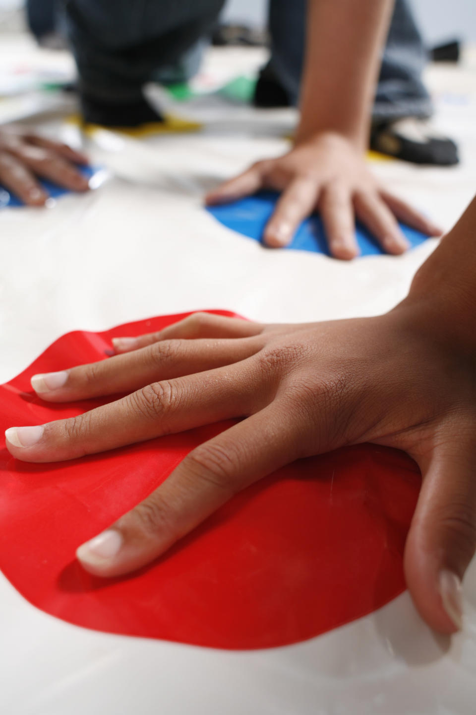 Hands being placed on various circles of color on a Twister game mat.